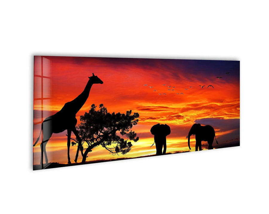 Sweeping across the panoramic glass printing, a warm sunset sky fills with flocks of birds in flight, animating the silhouettes of the giraffes and elephants of the safari.