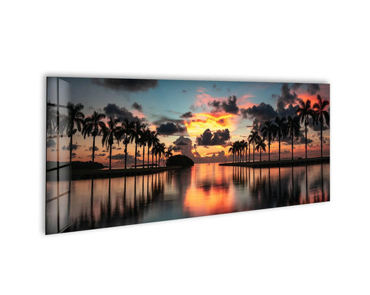 Miami Deering Estate sunrise glass wall art showcases a vibrant panoramic landscape and palm trees reflecting in calm water and dramatic clouds above sofa