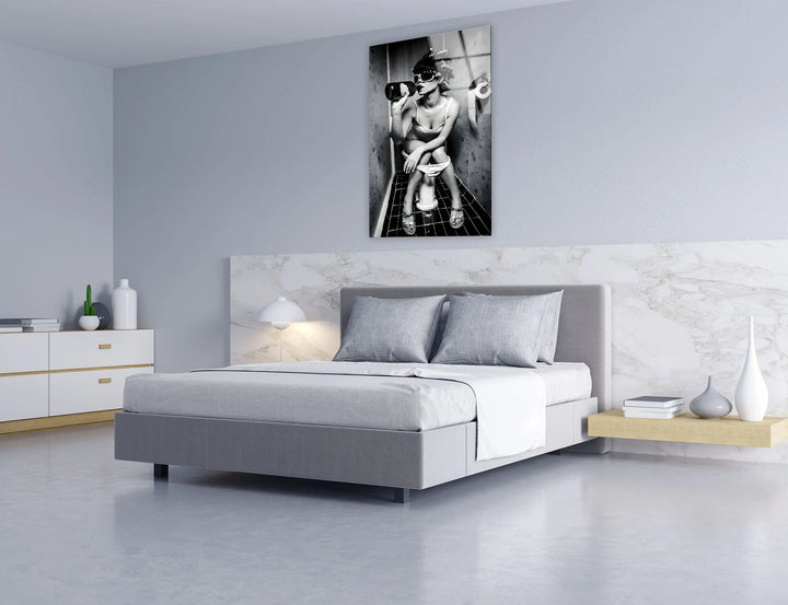 Glass wall art capturing a bold humorous moment of a woman sipping from a bottle in a narrow bathroom.