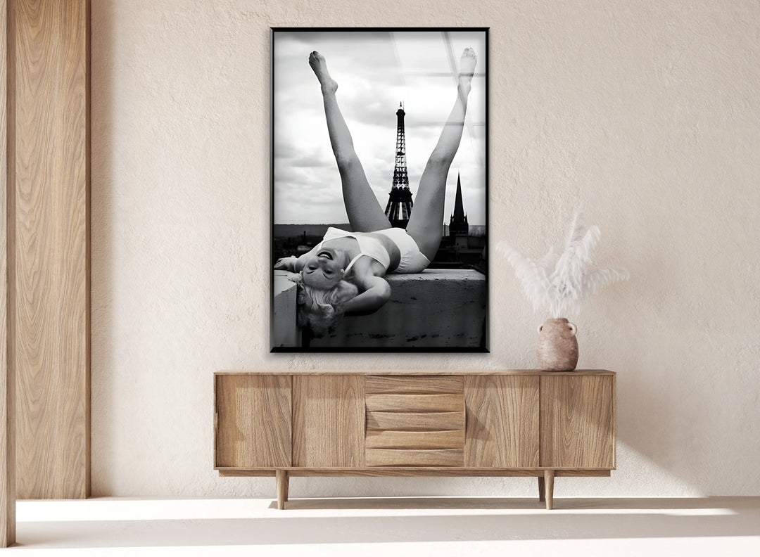 Monochrome glass panel showing a woman playfully lifting her legs against a Paris backdrop.