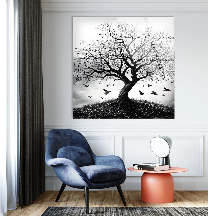 Grayscale glass wall art portraying a tree with scattered leaves and birds soaring into a moody sky.