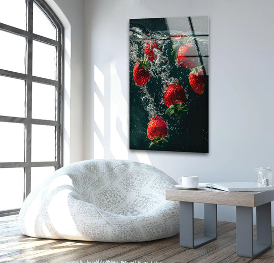 Vertical glass wall art featuring vibrant red strawberries submerged in water with bubbles against a dark background displayed above a sofa in a living room.