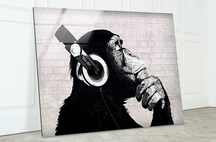 Banksy Dj Monkey Grayscale street-art–style image printed on glass of a chimp with headphones on a white brick wall.
