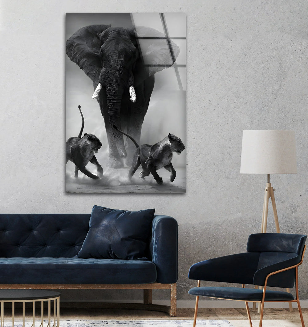 Monochrome wildlife glass art showing an elephant advancing behind two fleeing lions.