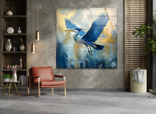 A blue heron with outstretched wings dominates this glass wall art, set against a dark abstract background featuring navy blues and gold accents.