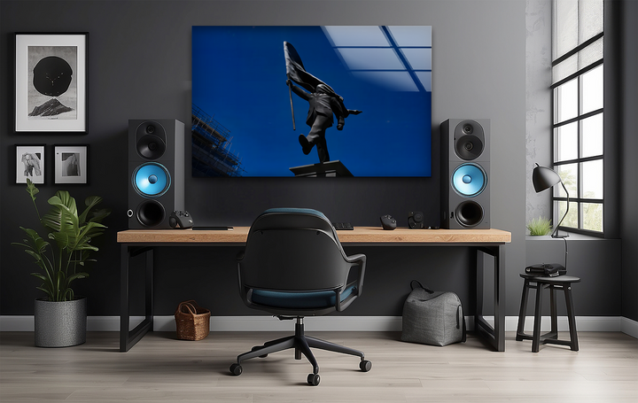 The striking color contrast in this tempered glass wall art highlights the dark flag bearer statue against a vibrant, deep blue sky.