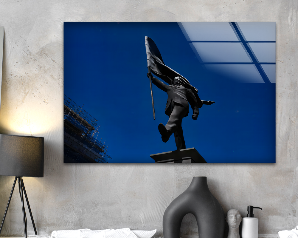 The transition from vibrant blue sky to the dark Banksy flag bearer, contrasted with the muted concrete wall, makes striking home decor.