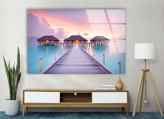Showcasing the layering effect, this tropical sunset glass print depicts a boardwalk leading to bungalows over turquoise waters, enriching your home decor.