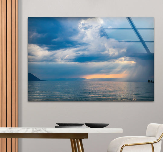 Stormy ocean sunset with dramatic sunlight is the loudest element in this decorative wall art glass print, creating a moody and vibrant sea landscape.