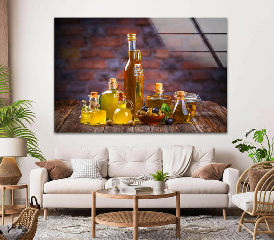 Horizontal glass wall art depicting a still life of oil bottles and olives displayed above a neutral sofa in a bright living room setting.