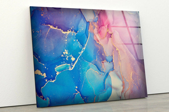 Abstract home decor featuring fluid pink and blue art with gold accents and a subtle grid reflection on the glass surface.