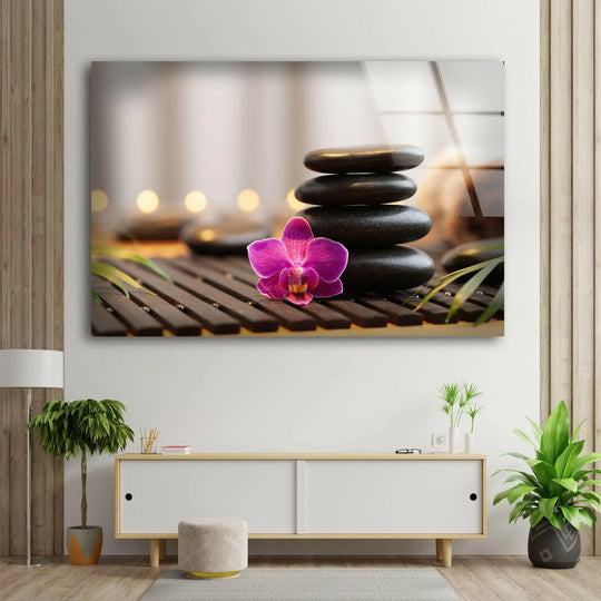 Abstract pink orchid and smooth zen stones on a dark wooden slat mat, captured in stunning glass wall artwork.