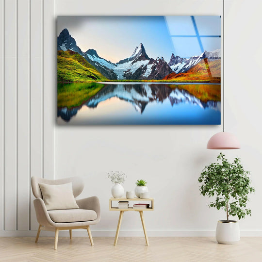 With vibrant color saturation, this sunrise mountain landscape glass print wall art showcases a stunning mirrored reflection of the alpine peaks and autumnal foliage.