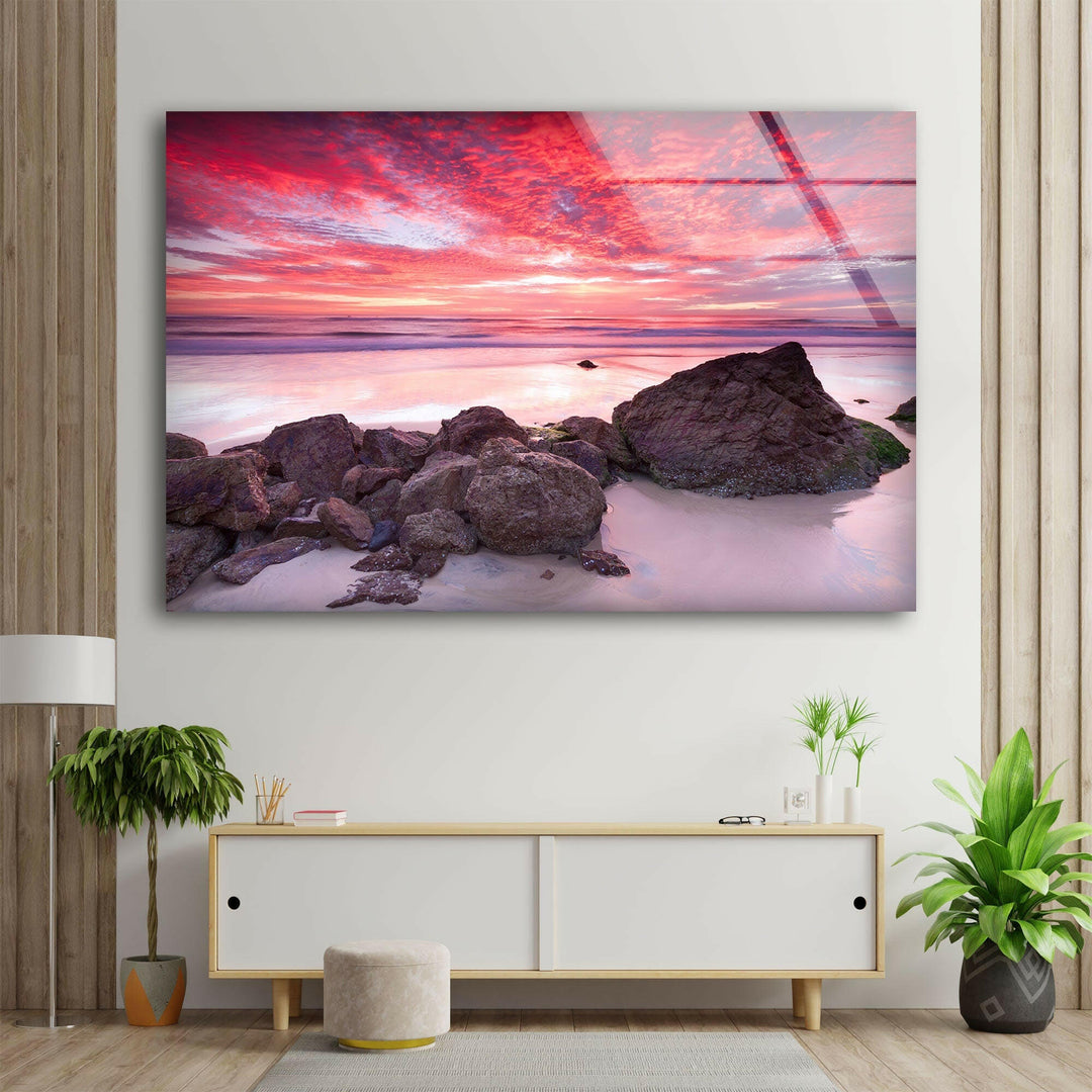 Dramatic sky reflecting on the ocean at sunset, framed by rocky formations.
