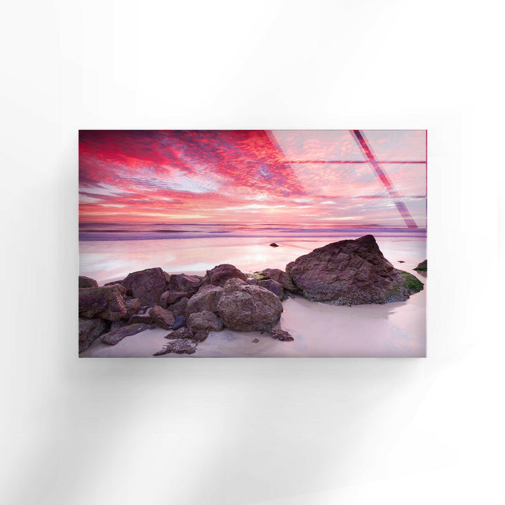 Serene seascape with glowing rocks and a vivid pink sunset in the background.
