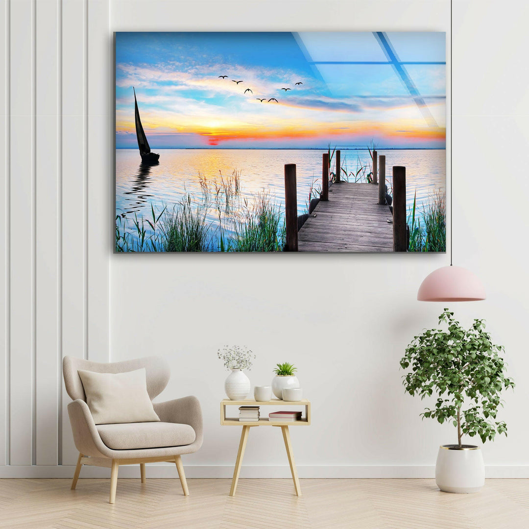 A breathtaking glass wall art of a serene lake pier with beautiful sunset hues reflecting on the water.
