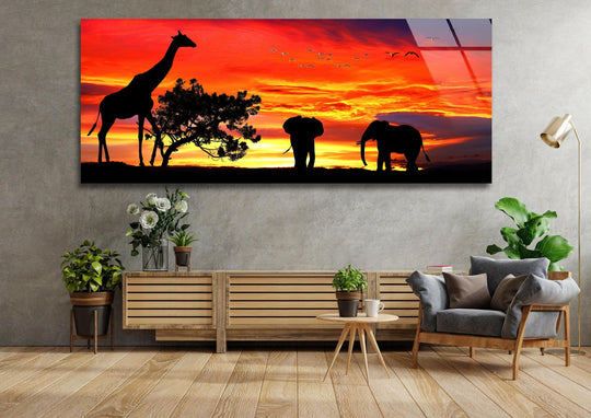 Safari Life glass wall art showcases a vibrant sunset and silhouetted giraffe and elephants and is a stunning panoramic piece of modern wall decor for a living room