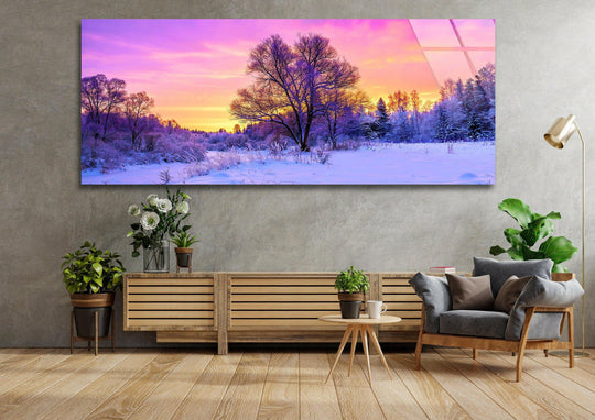 This panoramic glass wall art shows a snowy forest landscape with a vibrant sunset and bare trees and it is forest wall art for winter serenity decor