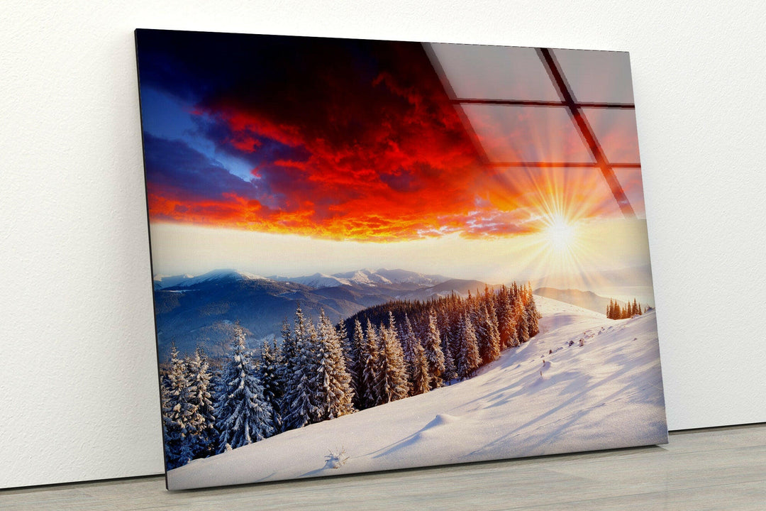 Vibrant winter sunset over a snowy mountain ridge with pine trees.
