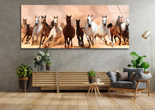 Running Horses In The Desert glass wall art showcases a dynamic scene and panoramic landscape with multiple horses and desert hues above a sofa