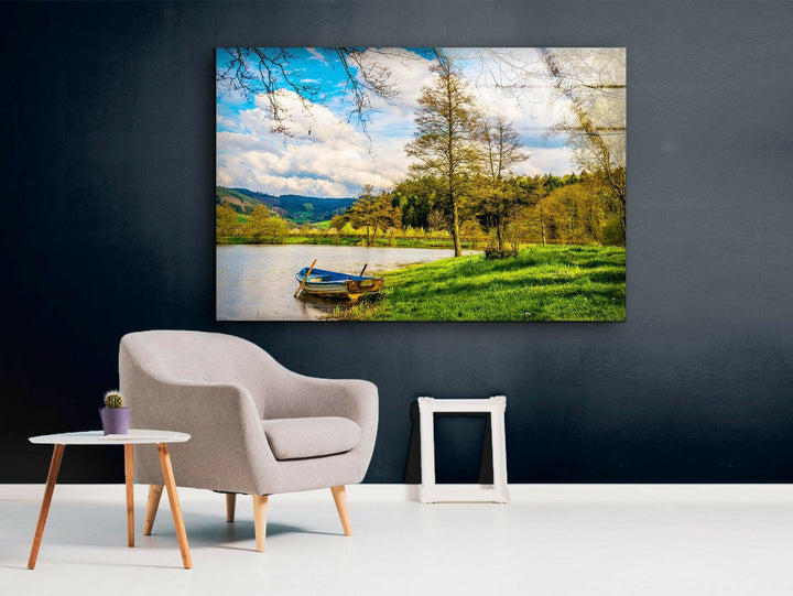 A peaceful river landscape with a wooden boat, blue sky, and green grass, printed on high-quality glass.
