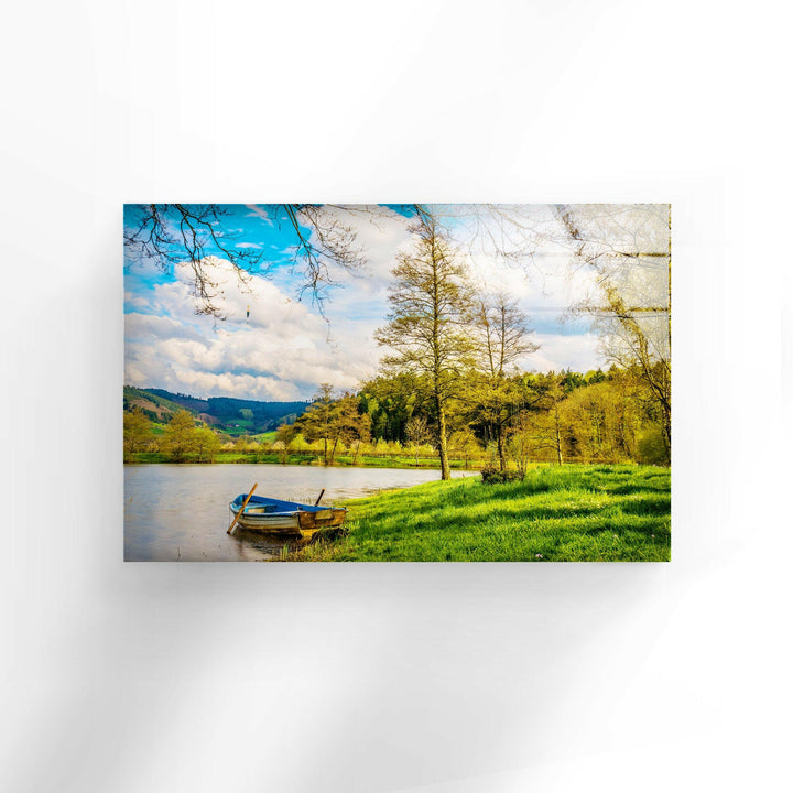 Breathtaking glass wall art depicting a peaceful riverside retreat with a wooden boat on still waters.
