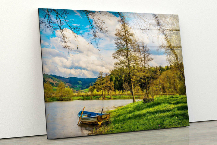 Nature-inspired glass wall art highlighting a charming wooden boat resting on a quiet riverbank.
