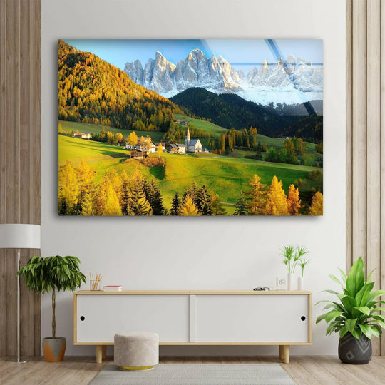 Warm light highlights the green valley and golden trees in this Val Di Funes landscape glass wall artwork, contrasting with the cool, snow-capped mountain peaks.