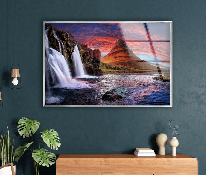 Serene mountain waterfall surrounded by lush greenery and a colorful sunset.
