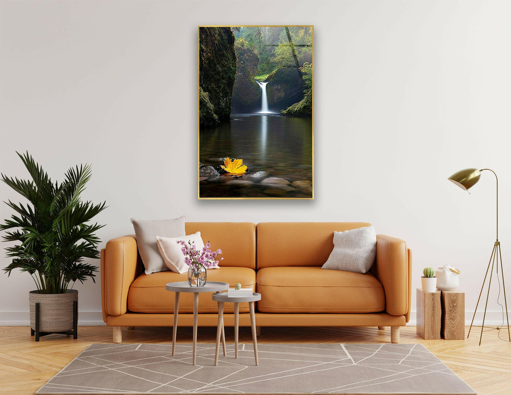 Breathtaking waterfall in a lush green forest with a golden autumn leaf on the water.
