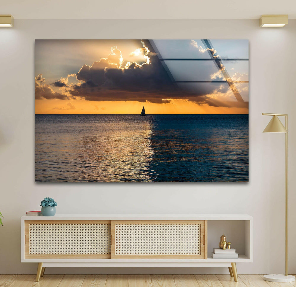 Glowing golden sunset over the calm sea, with a beautiful sailboat sailing across.
