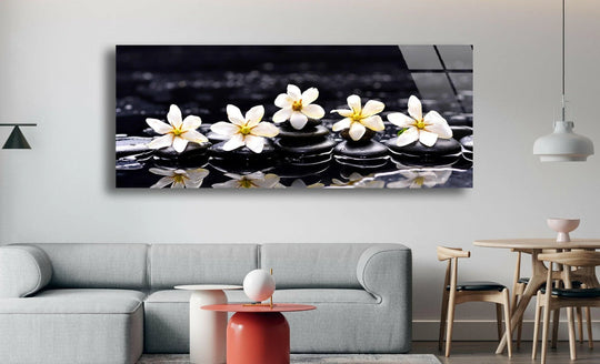 Gardenia With Therapy Stones glass wall art displays white flowers and black stones and offers spa serenity decor with a glossy finish and horizontal orientation above a sofa