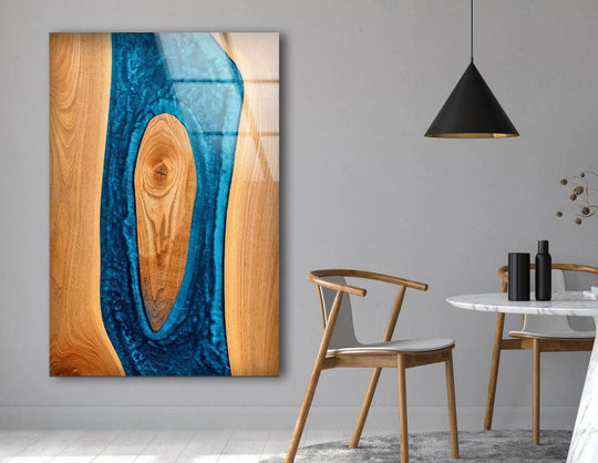 Close-up of a vibrant blue epoxy resin river flowing through warm wood grain on this glass wall artwork.