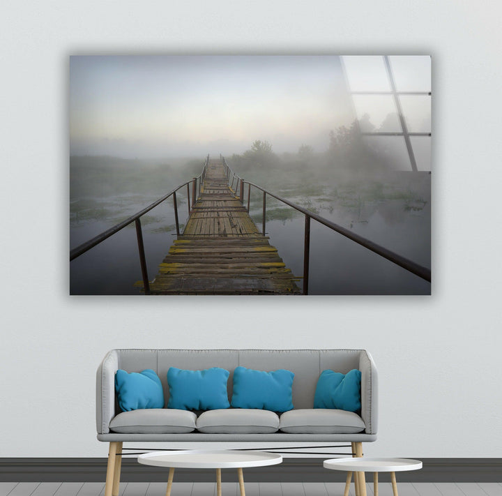 A rustic wooden bridge over a still body of water, enveloped in a dreamy mist.
