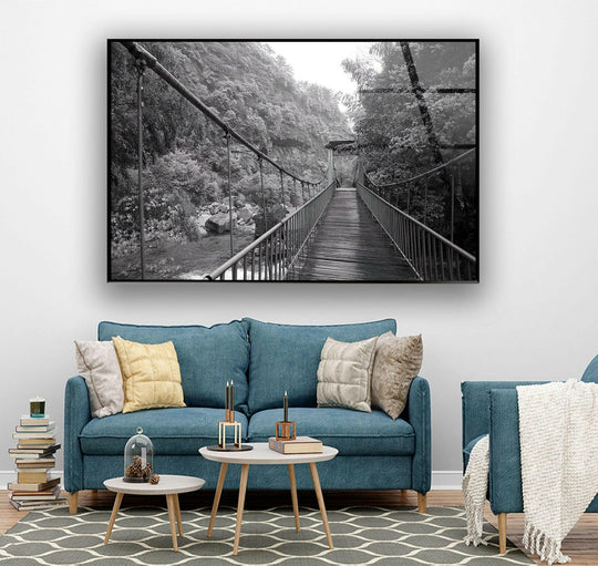 Glass wall art featuring a weathered suspension bridge creating organic lines within a verdant, rocky landscape.
