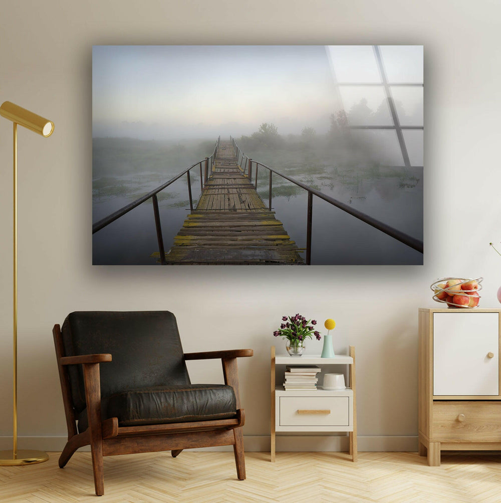 A misty wooden bridge stretching over calm water, surrounded by foggy scenery.
