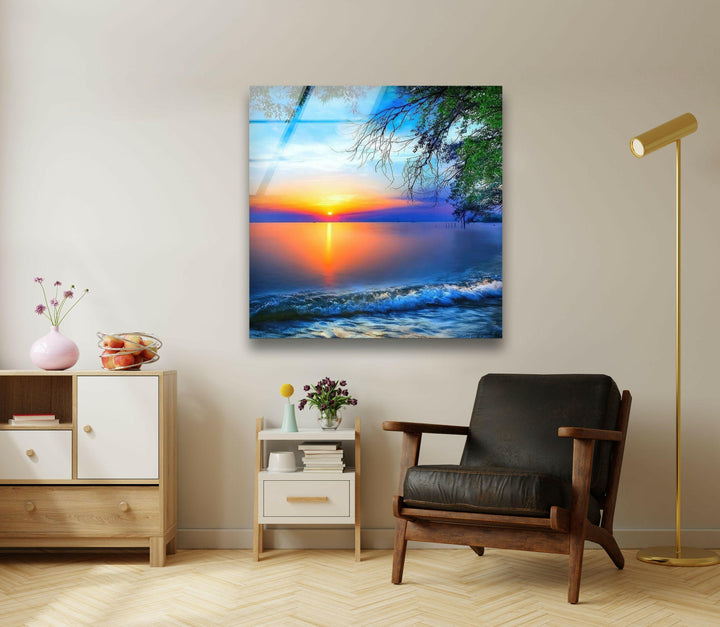 Golden sun setting over the sea with lush green branches framing the view on glass.
