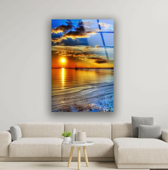 Glass wall art shows a golden sunset reflecting on calm waters and a serene pier reflecting coastal view and landscape themes