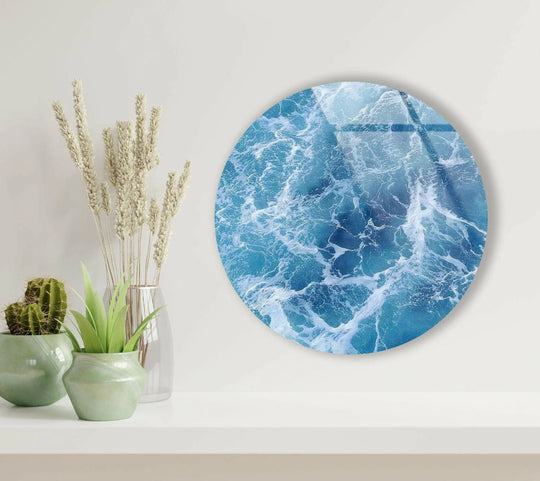 Round glass wall art shows blue ocean waves with white foam creating serene coastal decor and vibrant wall art on display