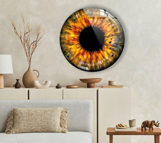 The high-gloss finish of this round glass wall art enhances the vibrant orange eye design, creating a unique modern wall decor piece.