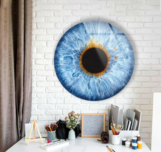 White negative space frames the realistic blue eye round glass printing, creating a captivating visual centerpiece on the textured brick wall above a tidy artist's desk.