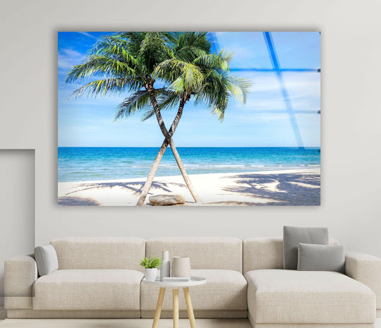 Featuring a clear, glossy finish, this tropical paradise palms print wall art on glass showcases two palm trees overlooking a beach with a blue ocean.