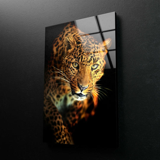 A close-up of a leopard's face, its intense yellow eyes the focal point of this striking glass wall art.