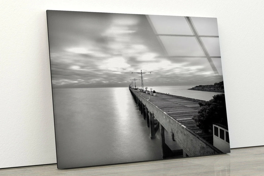 Tranquil black and white ocean scene with an aged pier leading into reflective water.