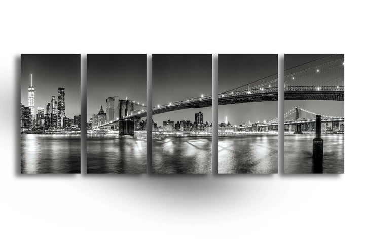 Panoramic black and white view of New York City lights and the Brooklyn Bridge.