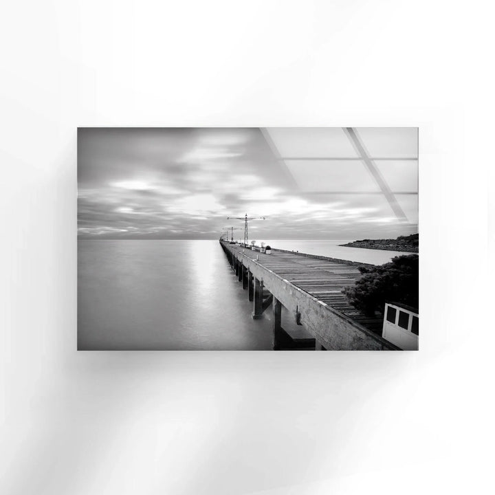 Minimalist coastal pier composition with smooth water and dramatic sky on glass wall art.